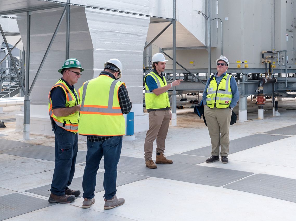 Workers in protective helmets and brightly colored work vests stand outside in a group
